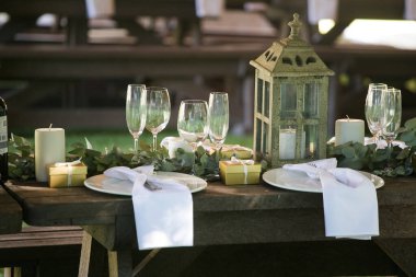 Bu büyüleyici görüntü, gerçek bir düğünün zarif dekorunu ve büyüleyici çiçek düzenlemelerini gözler önüne seriyor. Fotoğrafta zarif çiçekler, mumlar ve diğer dekoratif el ile süslenmiş büyüleyici bir düğün yerinde güzel dekore edilmiş bir masa yer alıyor.