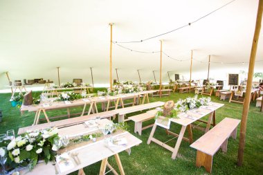 Bu büyüleyici görüntü, gerçek bir düğünün zarif dekorunu ve büyüleyici çiçek düzenlemelerini gözler önüne seriyor. Fotoğrafta zarif çiçekler, mumlar ve diğer dekoratif el ile süslenmiş büyüleyici bir düğün yerinde güzel dekore edilmiş bir masa yer alıyor.