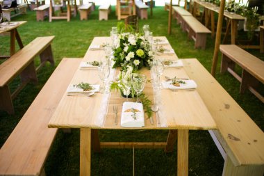 Bu büyüleyici görüntü, gerçek bir düğünün zarif dekorunu ve büyüleyici çiçek düzenlemelerini gözler önüne seriyor. Fotoğrafta zarif çiçekler, mumlar ve diğer dekoratif el ile süslenmiş büyüleyici bir düğün yerinde güzel dekore edilmiş bir masa yer alıyor.