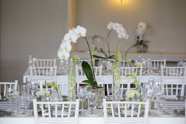 Bu büyüleyici görüntü, gerçek bir düğünün zarif dekorunu ve büyüleyici çiçek düzenlemelerini gözler önüne seriyor. Fotoğrafta zarif çiçekler, mumlar ve diğer dekoratif el ile süslenmiş büyüleyici bir düğün yerinde güzel dekore edilmiş bir masa yer alıyor.