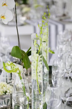 Bu büyüleyici görüntü, gerçek bir düğünün zarif dekorunu ve büyüleyici çiçek düzenlemelerini gözler önüne seriyor. Fotoğrafta zarif çiçekler, mumlar ve diğer dekoratif el ile süslenmiş büyüleyici bir düğün yerinde güzel dekore edilmiş bir masa yer alıyor.