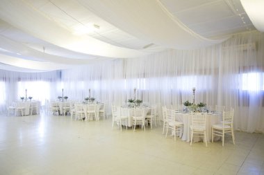 Bu büyüleyici görüntü, gerçek bir düğünün zarif dekorunu ve büyüleyici çiçek düzenlemelerini gözler önüne seriyor. Fotoğrafta zarif çiçekler, mumlar ve diğer dekoratif el ile süslenmiş büyüleyici bir düğün yerinde güzel dekore edilmiş bir masa yer alıyor.