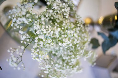 Bu büyüleyici görüntü, gerçek bir düğünün zarif dekorunu ve büyüleyici çiçek düzenlemelerini gözler önüne seriyor. Fotoğrafta zarif çiçekler, mumlar ve diğer dekoratif el ile süslenmiş büyüleyici bir düğün yerinde güzel dekore edilmiş bir masa yer alıyor.