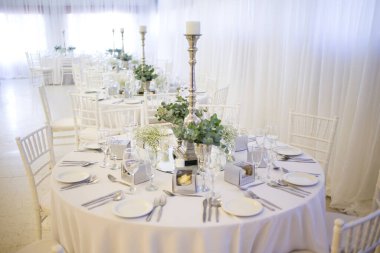 Bu büyüleyici görüntü, gerçek bir düğünün zarif dekorunu ve büyüleyici çiçek düzenlemelerini gözler önüne seriyor. Fotoğrafta zarif çiçekler, mumlar ve diğer dekoratif el ile süslenmiş büyüleyici bir düğün yerinde güzel dekore edilmiş bir masa yer alıyor.