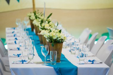 Bu büyüleyici görüntü, gerçek bir düğünün zarif dekorunu ve büyüleyici çiçek düzenlemelerini gözler önüne seriyor. Fotoğrafta zarif çiçekler, mumlar ve diğer dekoratif el ile süslenmiş büyüleyici bir düğün yerinde güzel dekore edilmiş bir masa yer alıyor.