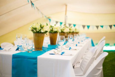 Bu büyüleyici görüntü, gerçek bir düğünün zarif dekorunu ve büyüleyici çiçek düzenlemelerini gözler önüne seriyor. Fotoğrafta zarif çiçekler, mumlar ve diğer dekoratif el ile süslenmiş büyüleyici bir düğün yerinde güzel dekore edilmiş bir masa yer alıyor.