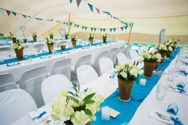 Bu büyüleyici görüntü, gerçek bir düğünün zarif dekorunu ve büyüleyici çiçek düzenlemelerini gözler önüne seriyor. Fotoğrafta zarif çiçekler, mumlar ve diğer dekoratif el ile süslenmiş büyüleyici bir düğün yerinde güzel dekore edilmiş bir masa yer alıyor.