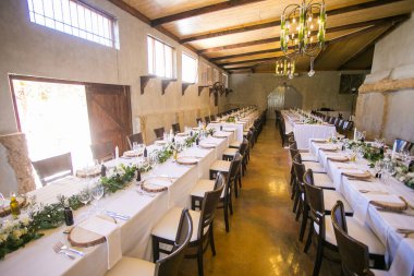 Bu büyüleyici görüntü, gerçek bir düğünün zarif dekorunu ve büyüleyici çiçek düzenlemelerini gözler önüne seriyor. Fotoğrafta zarif çiçekler, mumlar ve diğer dekoratif el ile süslenmiş büyüleyici bir düğün yerinde güzel dekore edilmiş bir masa yer alıyor.