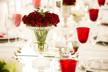 Bu büyüleyici görüntü, gerçek bir düğünün zarif dekorunu ve büyüleyici çiçek düzenlemelerini gözler önüne seriyor. Fotoğrafta zarif çiçekler, mumlar ve diğer dekoratif el ile süslenmiş büyüleyici bir düğün yerinde güzel dekore edilmiş bir masa yer alıyor.