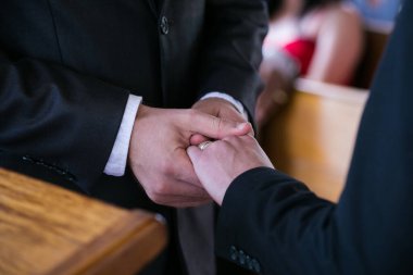 Bu güzel görüntü, bir çiftin gerçek bir düğünde yüzüklerini değiş tokuş ettiği samimi anı yakalıyor. Fotoğrafta çiftin ellerinin birbirine dolanmış parmaklarını ve parmaklarındaki alyansları gösteren yakın çekimi yer alıyor. Görüntü