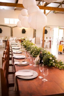 Bu büyüleyici görüntü, gerçek bir düğünün zarif dekorunu ve büyüleyici çiçek düzenlemelerini gözler önüne seriyor. Fotoğrafta zarif çiçekler, mumlar ve diğer dekoratif el ile süslenmiş büyüleyici bir düğün yerinde güzel dekore edilmiş bir masa yer alıyor.