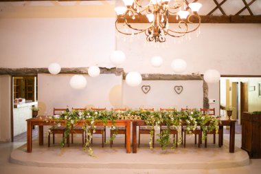 Bu büyüleyici görüntü, gerçek bir düğünün zarif dekorunu ve büyüleyici çiçek düzenlemelerini gözler önüne seriyor. Fotoğrafta zarif çiçekler, mumlar ve diğer dekoratif el ile süslenmiş büyüleyici bir düğün yerinde güzel dekore edilmiş bir masa yer alıyor.