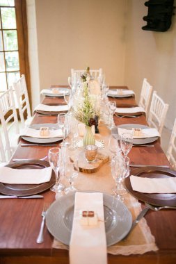 Bu büyüleyici görüntü, gerçek bir düğünün zarif dekorunu ve büyüleyici çiçek düzenlemelerini gözler önüne seriyor. Fotoğrafta zarif çiçekler, mumlar ve diğer dekoratif el ile süslenmiş büyüleyici bir düğün yerinde güzel dekore edilmiş bir masa yer alıyor.