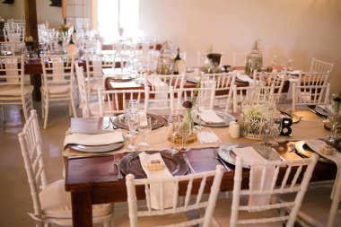 Bu büyüleyici görüntü, gerçek bir düğünün zarif dekorunu ve büyüleyici çiçek düzenlemelerini gözler önüne seriyor. Fotoğrafta zarif çiçekler, mumlar ve diğer dekoratif el ile süslenmiş büyüleyici bir düğün yerinde güzel dekore edilmiş bir masa yer alıyor.