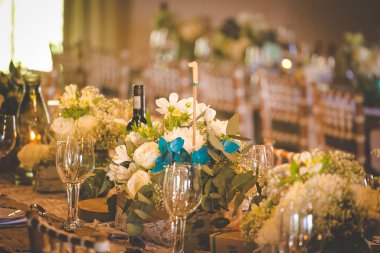 Bu büyüleyici görüntü, gerçek bir düğünün zarif dekorunu ve büyüleyici çiçek düzenlemelerini gözler önüne seriyor. Fotoğrafta zarif çiçekler, mumlar ve diğer dekoratif el ile süslenmiş büyüleyici bir düğün yerinde güzel dekore edilmiş bir masa yer alıyor.