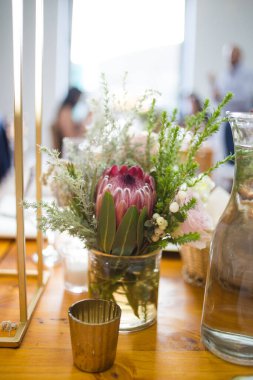 Bu büyüleyici görüntü, gerçek bir düğünün zarif dekorunu ve büyüleyici çiçek düzenlemelerini gözler önüne seriyor. Fotoğrafta zarif çiçekler, mumlar ve diğer dekoratif el ile süslenmiş büyüleyici bir düğün yerinde güzel dekore edilmiş bir masa yer alıyor.