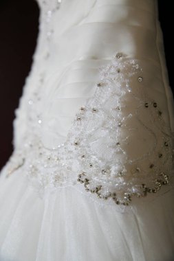 Bu büyüleyici görüntü, yaratıcı ve benzersiz bir şekilde fotoğraflanmış karmaşık detaylarla dolu bir gelinlik sergiliyor. Fotoğrafta karmaşık dantelli ve narin boncuklu çarpıcı beyaz bir gelinlik yer alıyor. Elbisenin fro fotografı var.