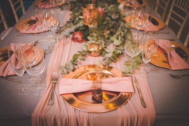 Bu büyüleyici görüntü, gerçek bir düğünün zarif dekorunu ve büyüleyici çiçek düzenlemelerini gözler önüne seriyor. Fotoğrafta zarif çiçekler, mumlar ve diğer dekoratif el ile süslenmiş büyüleyici bir düğün yerinde güzel dekore edilmiş bir masa yer alıyor.