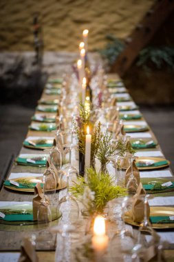 Bu büyüleyici görüntü, gerçek bir düğünün zarif dekorunu ve büyüleyici çiçek düzenlemelerini gözler önüne seriyor. Fotoğrafta zarif çiçekler, mumlar ve diğer dekoratif el ile süslenmiş büyüleyici bir düğün yerinde güzel dekore edilmiş bir masa yer alıyor.