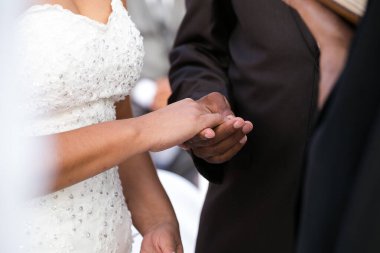 Bu güzel görüntü, bir çiftin gerçek bir düğünde yüzüklerini değiş tokuş ettiği samimi anı yakalıyor. Fotoğrafta çiftin ellerinin birbirine dolanmış parmaklarını ve parmaklarındaki alyansları gösteren yakın çekimi yer alıyor. Görüntü