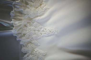 Bu büyüleyici görüntü, yaratıcı ve benzersiz bir şekilde fotoğraflanmış karmaşık detaylarla dolu bir gelinlik sergiliyor. Fotoğrafta karmaşık dantelli ve narin boncuklu çarpıcı beyaz bir gelinlik yer alıyor. Elbisenin fro fotografı var.