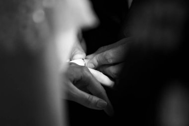 Bu güzel görüntü, bir çiftin gerçek bir düğünde yüzüklerini değiş tokuş ettiği samimi anı yakalıyor. Fotoğrafta çiftin ellerinin birbirine dolanmış parmaklarını ve parmaklarındaki alyansları gösteren yakın çekimi yer alıyor. Görüntü