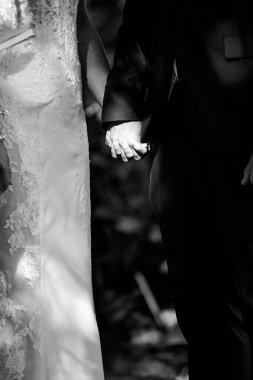 Bu güzel görüntü, bir çiftin gerçek bir düğünde yüzüklerini değiş tokuş ettiği samimi anı yakalıyor. Fotoğrafta çiftin ellerinin birbirine dolanmış parmaklarını ve parmaklarındaki alyansları gösteren yakın çekimi yer alıyor. Görüntü