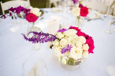 Bu büyüleyici görüntü, gerçek bir düğünün zarif dekorunu ve büyüleyici çiçek düzenlemelerini gözler önüne seriyor. Fotoğrafta zarif çiçekler, mumlar ve diğer dekoratif el ile süslenmiş büyüleyici bir düğün yerinde güzel dekore edilmiş bir masa yer alıyor.