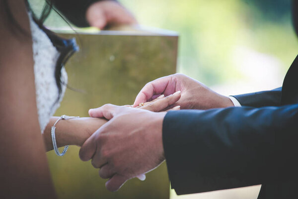 This beautiful image captures the intimate moment of a couple exchanging wedding rings at a real wedding. The photograph features a close-up of the couple's hands, showcasing their intertwined fingers and the wedding bands on their fingers. The image