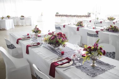 Bu büyüleyici görüntü, gerçek bir düğünün zarif dekorunu ve büyüleyici çiçek düzenlemelerini gözler önüne seriyor. Fotoğrafta zarif çiçekler, mumlar ve diğer dekoratif el ile süslenmiş büyüleyici bir düğün yerinde güzel dekore edilmiş bir masa yer alıyor.