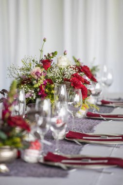 Bu büyüleyici görüntü, gerçek bir düğünün zarif dekorunu ve büyüleyici çiçek düzenlemelerini gözler önüne seriyor. Fotoğrafta zarif çiçekler, mumlar ve diğer dekoratif el ile süslenmiş büyüleyici bir düğün yerinde güzel dekore edilmiş bir masa yer alıyor.