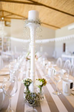 Bu büyüleyici görüntü, gerçek bir düğünün zarif dekorunu ve büyüleyici çiçek düzenlemelerini gözler önüne seriyor. Fotoğrafta zarif çiçekler, mumlar ve diğer dekoratif el ile süslenmiş büyüleyici bir düğün yerinde güzel dekore edilmiş bir masa yer alıyor.