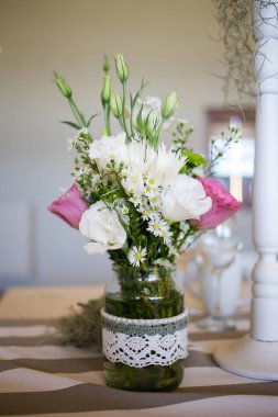 Bu büyüleyici görüntü, gerçek bir düğünün zarif dekorunu ve büyüleyici çiçek düzenlemelerini gözler önüne seriyor. Fotoğrafta zarif çiçekler, mumlar ve diğer dekoratif el ile süslenmiş büyüleyici bir düğün yerinde güzel dekore edilmiş bir masa yer alıyor.