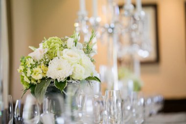 Bu büyüleyici görüntü, gerçek bir düğünün zarif dekorunu ve büyüleyici çiçek düzenlemelerini gözler önüne seriyor. Fotoğrafta zarif çiçekler, mumlar ve diğer dekoratif el ile süslenmiş büyüleyici bir düğün yerinde güzel dekore edilmiş bir masa yer alıyor.