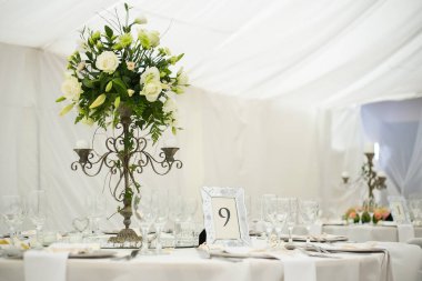 Bu büyüleyici görüntü, gerçek bir düğünün zarif dekorunu ve büyüleyici çiçek düzenlemelerini gözler önüne seriyor. Fotoğrafta zarif çiçekler, mumlar ve diğer dekoratif el ile süslenmiş büyüleyici bir düğün yerinde güzel dekore edilmiş bir masa yer alıyor.