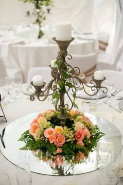 Bu büyüleyici görüntü, gerçek bir düğünün zarif dekorunu ve büyüleyici çiçek düzenlemelerini gözler önüne seriyor. Fotoğrafta zarif çiçekler, mumlar ve diğer dekoratif el ile süslenmiş büyüleyici bir düğün yerinde güzel dekore edilmiş bir masa yer alıyor.