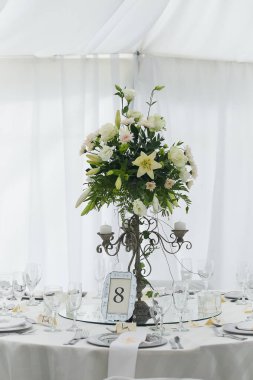 Bu büyüleyici görüntü, gerçek bir düğünün zarif dekorunu ve büyüleyici çiçek düzenlemelerini gözler önüne seriyor. Fotoğrafta zarif çiçekler, mumlar ve diğer dekoratif el ile süslenmiş büyüleyici bir düğün yerinde güzel dekore edilmiş bir masa yer alıyor.