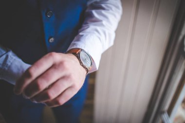 Bu büyüleyici görüntü, damadın büyük günü için giyinirken takım elbisesi, ayakkabıları ve kol düğmeleri de dahil olmak üzere düğün kıyafetini gösteriyor. Fotoğraf, damadın kıyafetinin karmaşık detaylarını vurguluyor. Güzel bir kompozisyon oluşturuyor. 