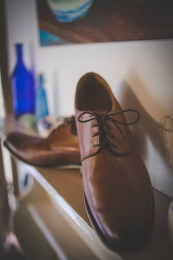 Bu büyüleyici görüntü, damadın büyük günü için giyinirken takım elbisesi, ayakkabıları ve kol düğmeleri de dahil olmak üzere düğün kıyafetini gösteriyor. Fotoğraf, damadın kıyafetinin karmaşık detaylarını vurguluyor. Güzel bir kompozisyon oluşturuyor. 