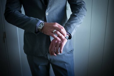 Bu büyüleyici görüntü, damadın büyük günü için giyinirken takım elbisesi, ayakkabıları ve kol düğmeleri de dahil olmak üzere düğün kıyafetini gösteriyor. Fotoğraf, damadın kıyafetinin karmaşık detaylarını vurguluyor. Güzel bir kompozisyon oluşturuyor. 