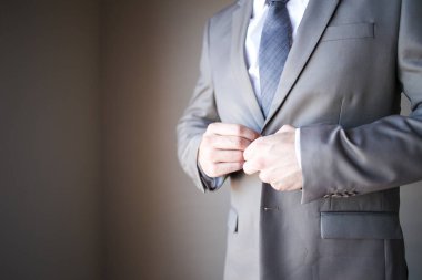 Bu büyüleyici görüntü, damadın büyük günü için giyinirken takım elbisesi, ayakkabıları ve kol düğmeleri de dahil olmak üzere düğün kıyafetini gösteriyor. Fotoğraf, damadın kıyafetinin karmaşık detaylarını vurguluyor. Güzel bir kompozisyon oluşturuyor. 