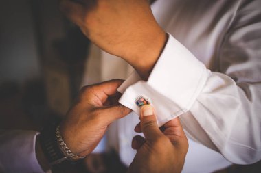 Bu büyüleyici görüntü, damadın büyük günü için giyinirken takım elbisesi, ayakkabıları ve kol düğmeleri de dahil olmak üzere düğün kıyafetini gösteriyor. Fotoğraf, damadın kıyafetinin karmaşık detaylarını vurguluyor. Güzel bir kompozisyon oluşturuyor. 