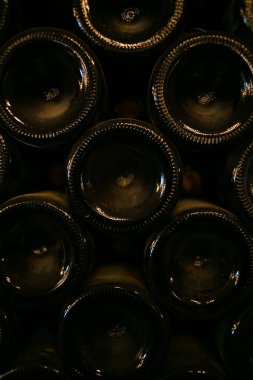 Şarap mahzeninde bir yığın şarap şişesi. Şişeler farklı şekil ve boyutlarda, ve hepsi görüntüyü öne çıkaracak şekilde düzenlenmiş. Şişelerin hepsi farklı renkte ve şekillerde, ve hepsi farklı şekillerde dizilmiş.