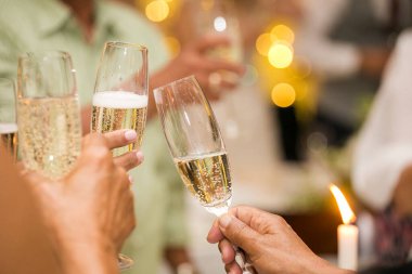 Düğünde şampanya bardaklarıyla tezahürat yapan bir grup insan. Gözlük ve ellere odaklanmış durumda. İnsanlar gülümsüyor ve mutlu görünüyorlar..