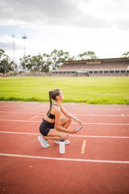 Stadyum ortamında hazırlık, susuzluk ve kararlılık gösterirken pistteki eğitimi sırasında yakalanmış odaklanmış bir bayan atlet. Zindelik, motivasyon ve atletik performansı vurgular.