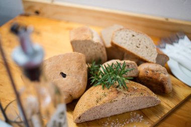 Ahşap bir tahtada servis edilen taze pişmiş zanaatkar ekmeği, biberiye filizi ve kaba tuz ile süslenmiş, kırsal ve davetkar bir sunum yaratıyor..