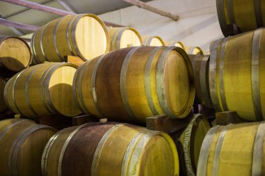 Şarap mahzeninde istiflenmiş ahşap şarap fıçıları, geleneksel şarap yaşlanmalarını ve kontrollü bir çevredeki depolama uygulamalarını vurguluyor..