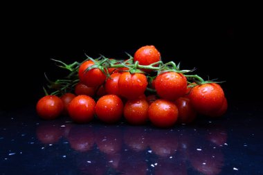 Yeşil saplı taze, kırmızı domatesler koyu arkaplanda kiraz domatesleri.