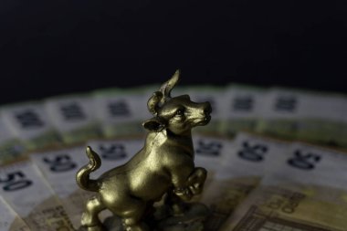 A miniature model of a bull with banknotes on black background Business concept, stock exchange, finance bull money
