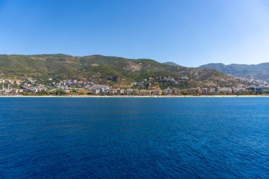 Alanya, Antalya - Türkiye 08: 11 2023: Alanya yarımadası, Antalya, Türkiye 'de deniz ve kayalarla kaplı Kleopatra Sahili. Yüksek yeşil uçurumu ve Alanya Kalesi olan güzel bir turizm manzarası..